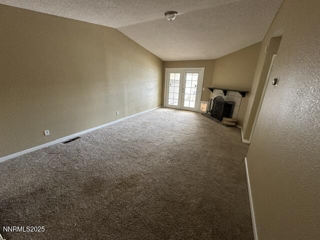 10083 Zeolite Dr, Reno, NV 89506 - unfurnished living room with a textured wall, a textured ceiling, vaulted ceiling, a fireplace with raised hearth, and carpet floors