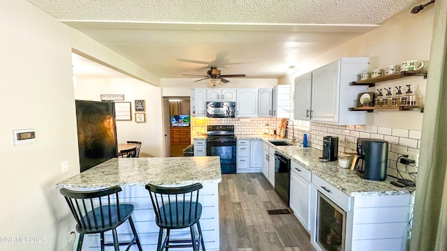 241 W National Ave, Winnemucca, NV 89445 - kitchen featuring black appliances, a peninsula, a kitchen bar, wood finished floors, and decorative backsplash