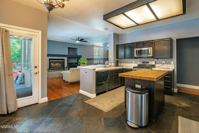 1500 Backer Way, Reno, NV 89523 - kitchen featuring appliances with stainless steel finishes, wooden counters, a peninsula, dark stone finish flooring, and a glass covered fireplace