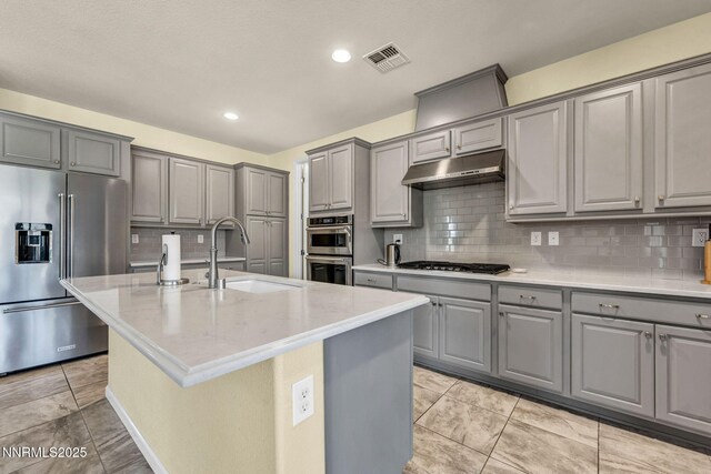 2222 Nasrullah Ln, Reno, NV 89521 - kitchen with gray cabinets, stainless steel appliances, under cabinet range hood, tasteful backsplash, and a kitchen island with sink