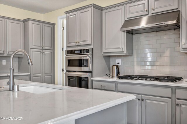 2222 Nasrullah Ln, Reno, NV 89521 - kitchen featuring under cabinet range hood, gray cabinetry, stainless steel appliances, decorative backsplash, and light stone counters