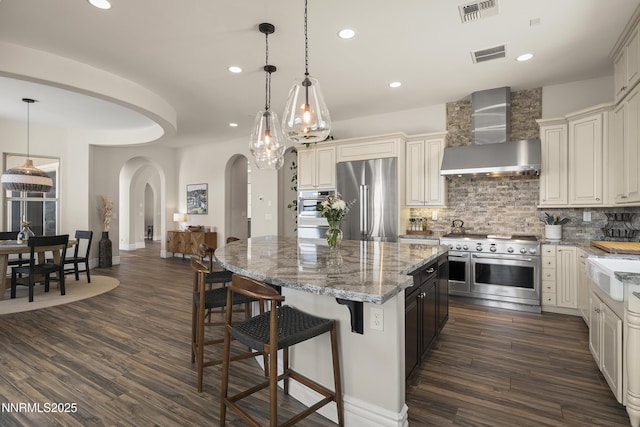 5427 Salmon River Ct, Reno, NV 89511 - kitchen with wall chimney exhaust hood, high quality appliances, arched walkways, a center island, and decorative backsplash