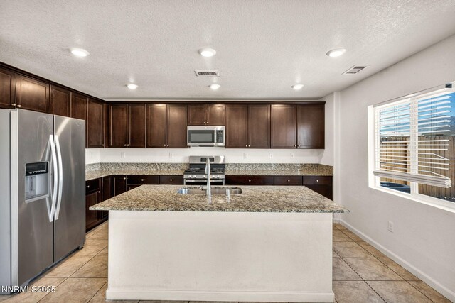 8977 Sagemoor Dr, Reno, NV 89506 - kitchen with appliances with stainless steel finishes, light tile patterned flooring, light stone countertops, dark brown cabinets, and an island with sink