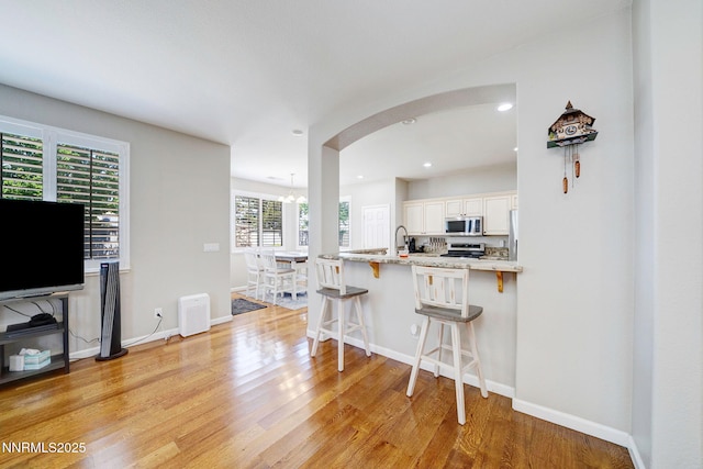 1575 Canyonlands Ct, Reno, NV 89521 - kitchen with stainless steel microwave, a kitchen bar, light wood-style flooring, arched walkways, and recessed lighting