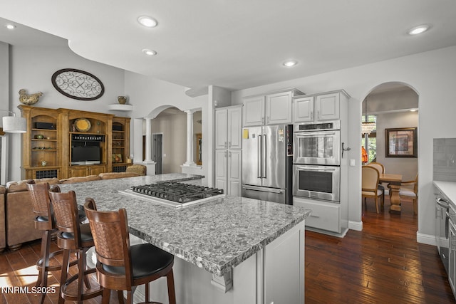 4374 Cullen Ct, Reno, NV 89519 - kitchen featuring stainless steel appliances, decorative columns, arched walkways, dark wood-style flooring, and a center island