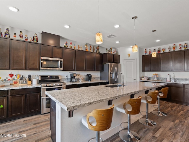 2217 Millville Dr, Spanish Springs, NV 89441 - kitchen with stainless steel appliances, wood finished floors, dark brown cabinetry, an island with sink, and a breakfast bar