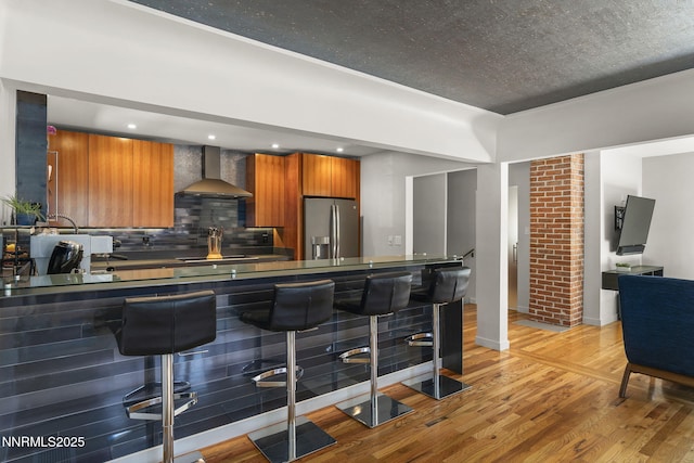 1296 Nixon Ave, Reno, NV 89509 - kitchen featuring stainless steel refrigerator with ice dispenser, wall chimney exhaust hood, brown cabinetry, and light wood-style floors