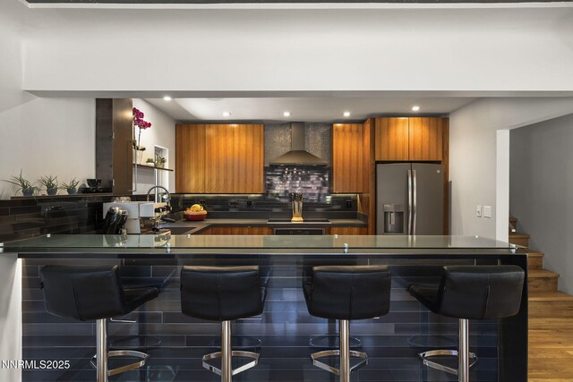 1296 Nixon Ave, Reno, NV 89509 - kitchen featuring stainless steel fridge, wall chimney range hood, brown cabinetry, dark countertops, and a peninsula