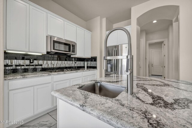 11575 Anthem Dr, Spanish Springs, NV 89441 - kitchen featuring stainless steel appliances, white cabinetry, light stone counters, arched walkways, and light marble finish floors