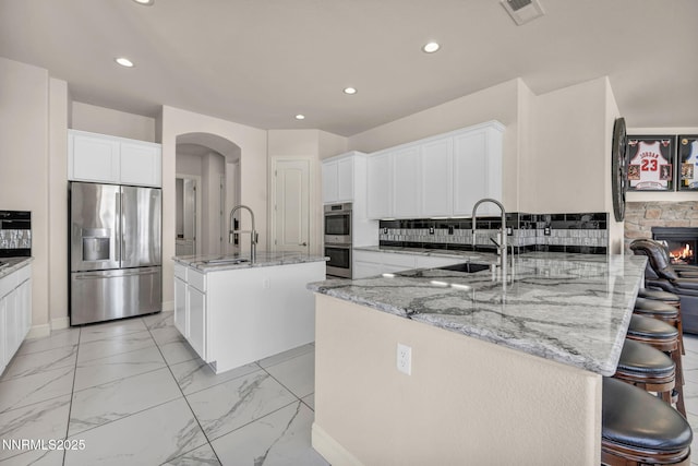 11575 Anthem Dr, Spanish Springs, NV 89441 - kitchen featuring stainless steel appliances, light stone counters, a peninsula, arched walkways, and recessed lighting