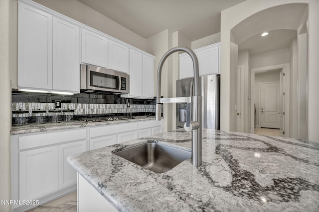 11575 Anthem Dr, Spanish Springs, NV 89441 - kitchen with stainless steel appliances, white cabinetry, arched walkways, light stone counters, and tasteful backsplash