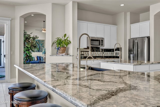 11575 Anthem Dr, Spanish Springs, NV 89441 - kitchen featuring appliances with stainless steel finishes, a ceiling fan, light stone countertops, white cabinets, and a breakfast bar area