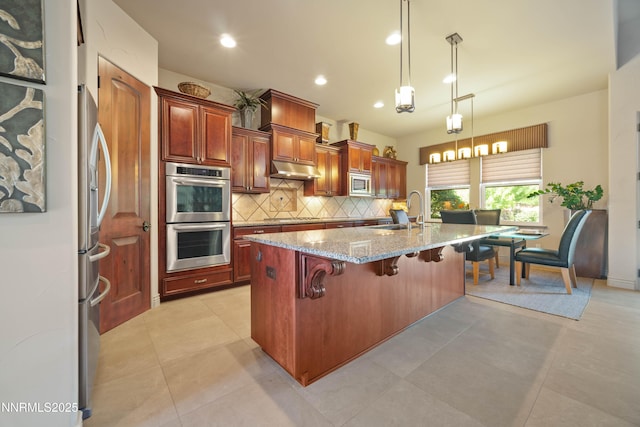 3970 Nature Trl, Reno, NV 89511 - kitchen featuring appliances with stainless steel finishes, backsplash, a breakfast bar area, light stone countertops, and an island with sink