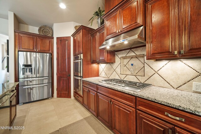 3970 Nature Trl, Reno, NV 89511 - kitchen featuring appliances with stainless steel finishes, exhaust hood, decorative backsplash, light stone counters, and reddish brown cabinets