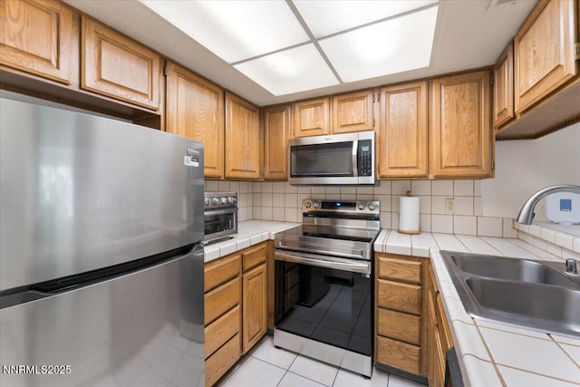 3095 Lakeside Dr # 103, Reno, NV 89509 - kitchen with appliances with stainless steel finishes, tile counters, light tile patterned flooring, decorative backsplash, and brown cabinetry