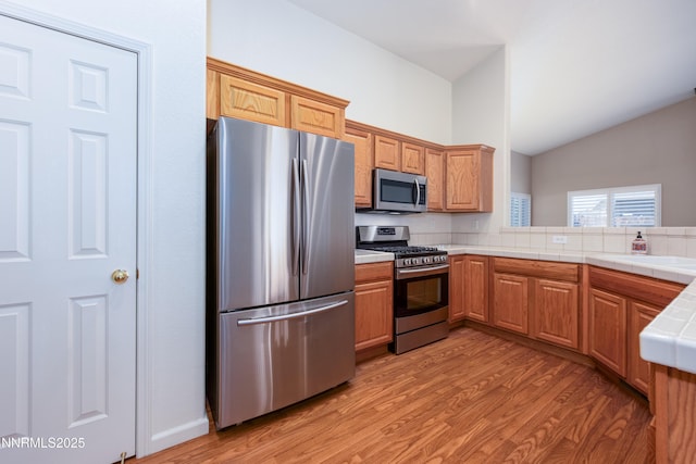 1421 Chiltern Ct, Gardnerville, NV 89410 - kitchen featuring appliances with stainless steel finishes, light wood finished floors, lofted ceiling, tile countertops, and a peninsula