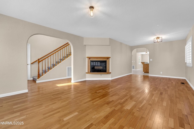 979 University Ridge Dr, Reno, NV 89512 - unfurnished living room featuring arched walkways, light wood finished floors, a glass covered fireplace, and stairs