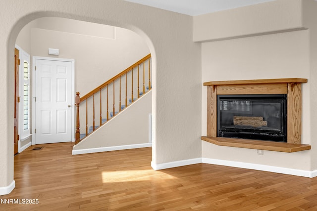 979 University Ridge Dr, Reno, NV 89512 - unfurnished living room with arched walkways, wood finished floors, a glass covered fireplace, and stairway