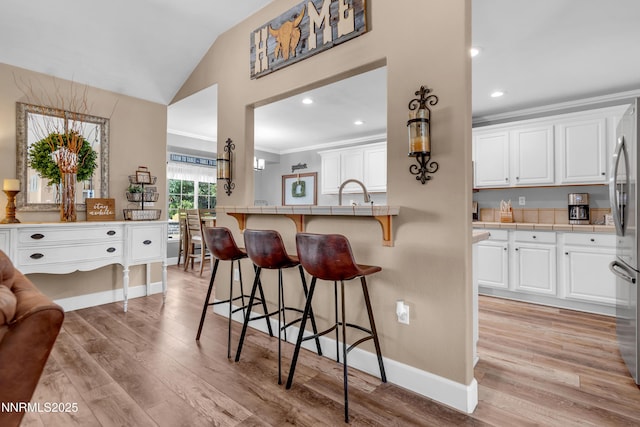 1450 Talon Ct, Spanish Springs, NV 89441 - kitchen featuring tile counters, a kitchen breakfast bar, lofted ceiling, white cabinets, and light wood-type flooring
