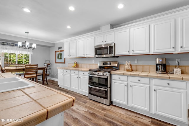 1450 Talon Ct, Spanish Springs, NV 89441 - kitchen with appliances with stainless steel finishes, white cabinets, crown molding, a chandelier, and light wood-type flooring