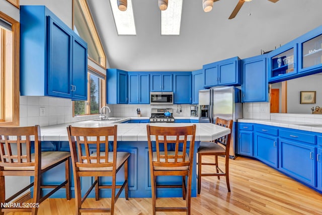 1008 Georgia Ln, Gardnerville, NV 89460 - kitchen with appliances with stainless steel finishes, tile counters, blue cabinetry, a peninsula, and vaulted ceiling