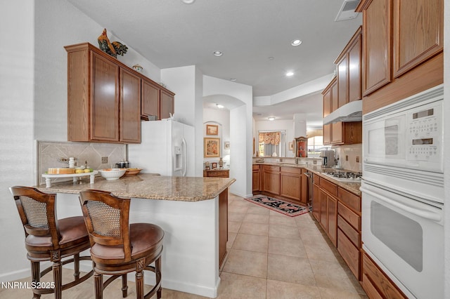 9900 Wilbur May Pkwy Unit 2001, Reno, NV 89521 - kitchen featuring white appliances, a peninsula, decorative backsplash, light stone countertops, and recessed lighting