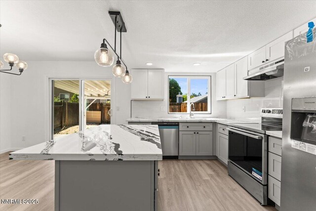 2719 Chavez Dr, Reno, NV 89502 - kitchen with under cabinet range hood, appliances with stainless steel finishes, gray cabinetry, light wood finished floors, and light stone counters
