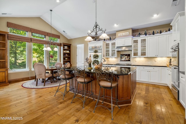16956 Rue Du Parc Ave, Reno, NV 89511 - kitchen with vaulted ceiling, light wood-style floors, appliances with stainless steel finishes, white cabinetry, and a kitchen bar