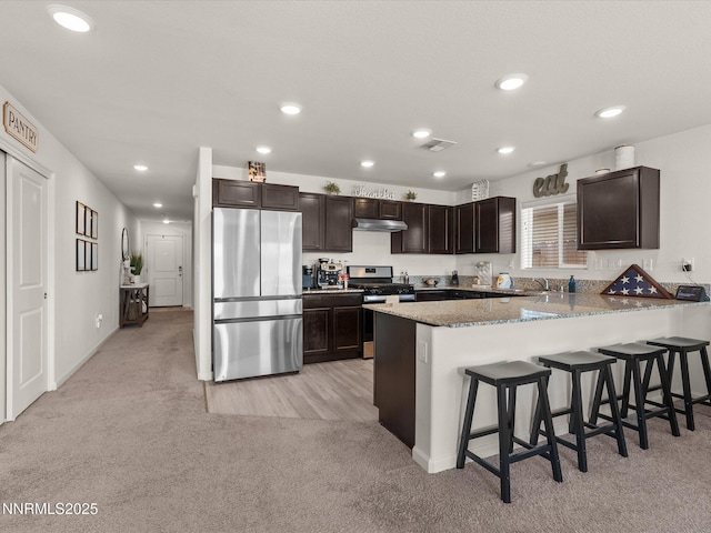 9237 Logan Creek Rd, Reno, NV 89506 - kitchen featuring appliances with stainless steel finishes, light carpet, dark brown cabinets, a kitchen bar, and recessed lighting