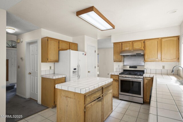 940 Skyway Dr, Reno, NV 89523 - kitchen with gas stove, white refrigerator with ice dispenser, under cabinet range hood, tile countertops, and light tile patterned floors