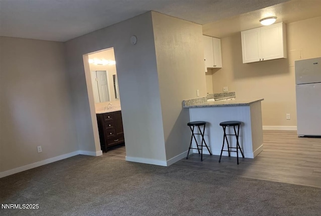 2450 Lymbery St Apt 107, Reno, NV 89509 - kitchen with freestanding refrigerator, white cabinets, carpet floors, a kitchen bar, and a peninsula