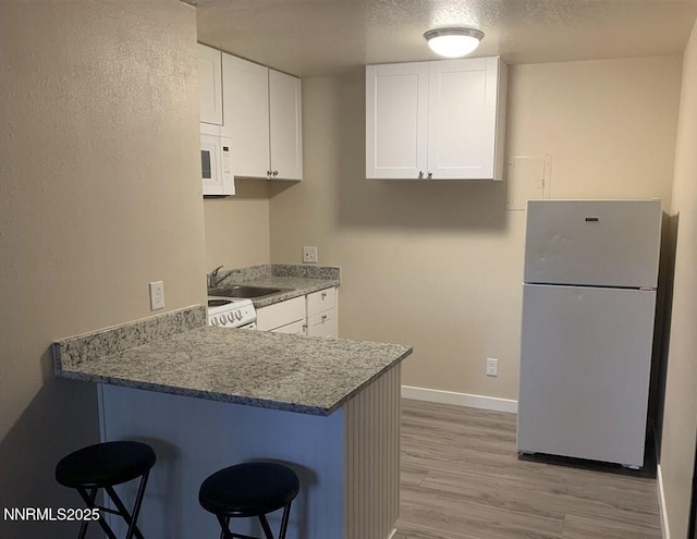 2450 Lymbery St Apt 107, Reno, NV 89509 - kitchen featuring white appliances, a kitchen breakfast bar, a peninsula, white cabinets, and light wood-type flooring