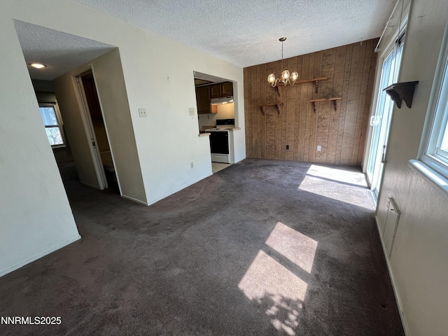 972 Flatcar Ln, Sparks, NV 89431 - unfurnished living room featuring a textured ceiling, a chandelier, dark carpet, wood walls, and healthy amount of natural light