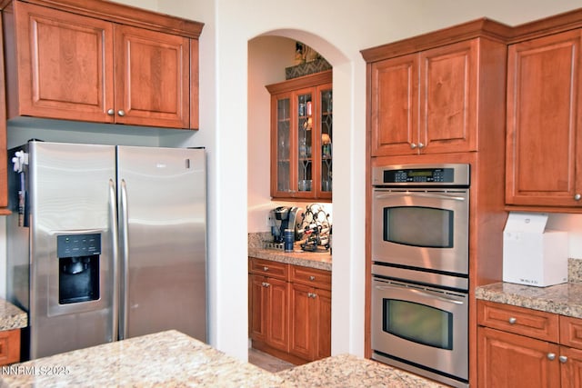 15180 Redmond Lp, Reno, NV 89511 - kitchen featuring stainless steel appliances, light stone counters, brown cabinetry, and arched walkways