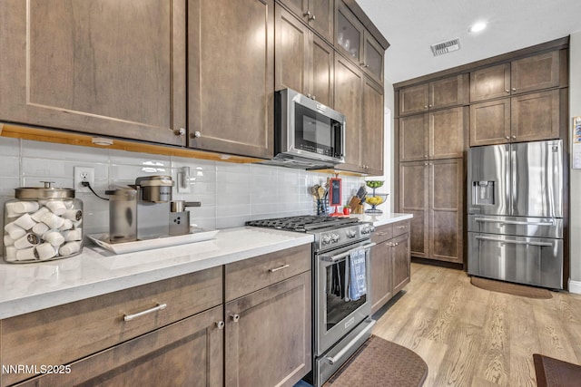 2109 Cast Iron Dr, Reno, NV 89521 - kitchen featuring appliances with stainless steel finishes, light wood-style floors, decorative backsplash, light stone countertops, and recessed lighting