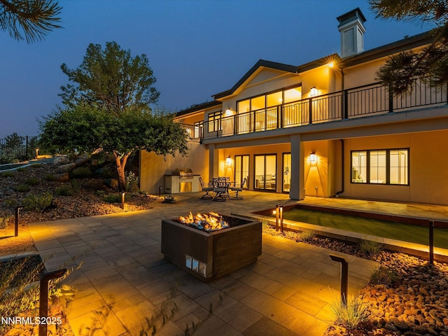 3662 Spirit Bluff Ct, Reno, NV 89511 - back of house at twilight with a balcony, a patio area, an outdoor fire pit, and stucco siding