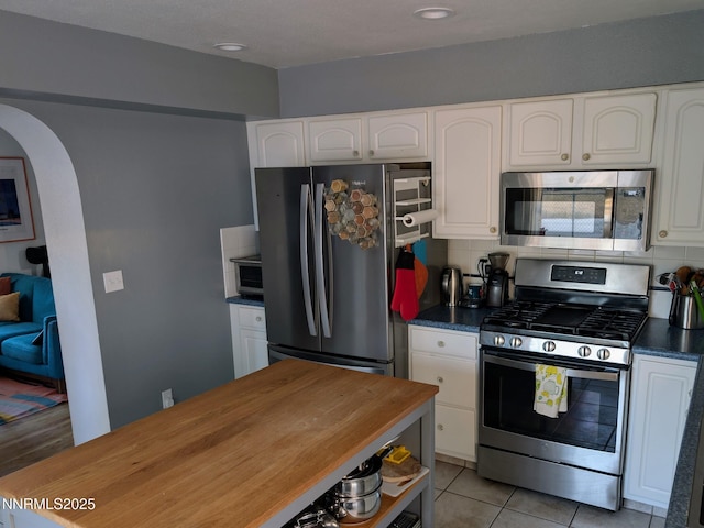 1640 Liston Ave, Reno, NV 89502 - kitchen featuring appliances with stainless steel finishes, arched walkways, white cabinets, decorative backsplash, and light tile patterned flooring