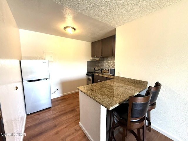2450 Lymbery St Unit 219, Reno, NV 89509 - kitchen with freestanding refrigerator, stainless steel range with gas cooktop, a textured ceiling, under cabinet range hood, and a peninsula