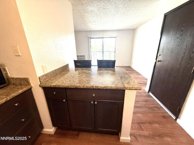 2450 Lymbery St Unit 219, Reno, NV 89509 - kitchen featuring a peninsula, dark wood-style flooring, light stone counters, a textured ceiling, and dark brown cabinets