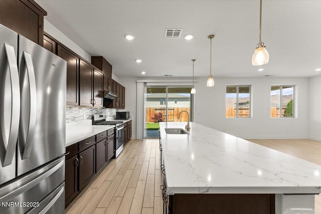 2251 Slater Mill Dr, Sparks, NV 89441 - kitchen with stainless steel appliances, light wood-type flooring, a kitchen island with sink, decorative backsplash, and dark brown cabinets