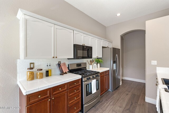 10265 Donnay Ct, Reno, NV 89521 - kitchen featuring appliances with stainless steel finishes, arched walkways, light wood-style flooring, white cabinetry, and tasteful backsplash