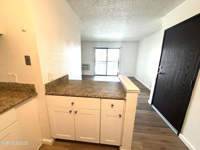 2450 Lymbery St Unit 228, Reno, NV 89509 - kitchen featuring a peninsula, dark wood finished floors, a textured ceiling, white cabinets, and a wall unit AC