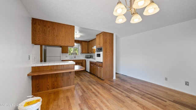 908 E Robinson St, Carson City, NV 89701 - kitchen with white appliances, a peninsula, wood finished floors, brown cabinetry, and decorative backsplash
