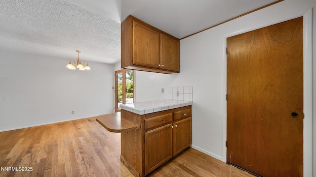 908 E Robinson St, Carson City, NV 89701 - kitchen featuring brown cabinetry, light wood-style floors, a chandelier, tile countertops, and decorative light fixtures