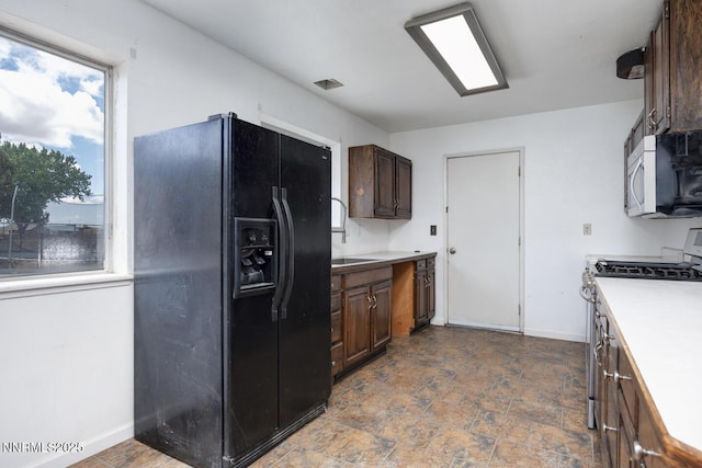 1021 Whitaker Ln, Fallon, NV 89406 - kitchen with black refrigerator with ice dispenser, stainless steel gas range, dark brown cabinetry, light countertops, and dark stone finish floors