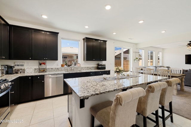 1149 Dapple Dr, Minden, NV 89423 - kitchen featuring stainless steel appliances, open floor plan, light tile patterned floors, light stone counters, and a kitchen bar
