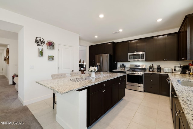 1149 Dapple Dr, Minden, NV 89423 - kitchen featuring stainless steel appliances, a kitchen island, a kitchen breakfast bar, light tile patterned floors, and light stone countertops