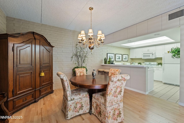 1200 Riverside Dr # 1232, Reno, NV 89503 - dining space with brick wall, light wood-style floors, a chandelier, a textured ceiling, and a skylight