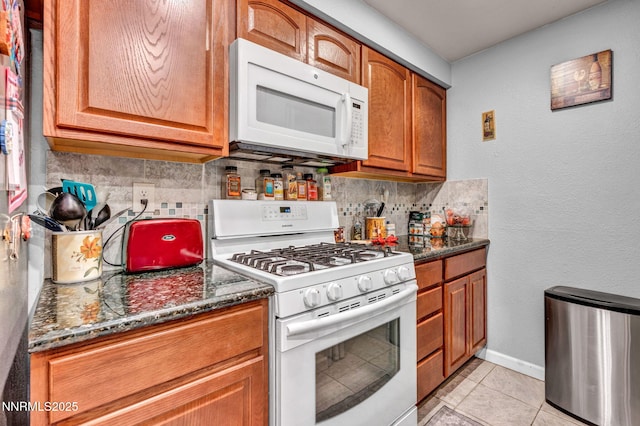 6670 Lotus St, Reno, NV 89506 - kitchen featuring white appliances, tasteful backsplash, brown cabinets, light tile patterned floors, and dark stone countertops