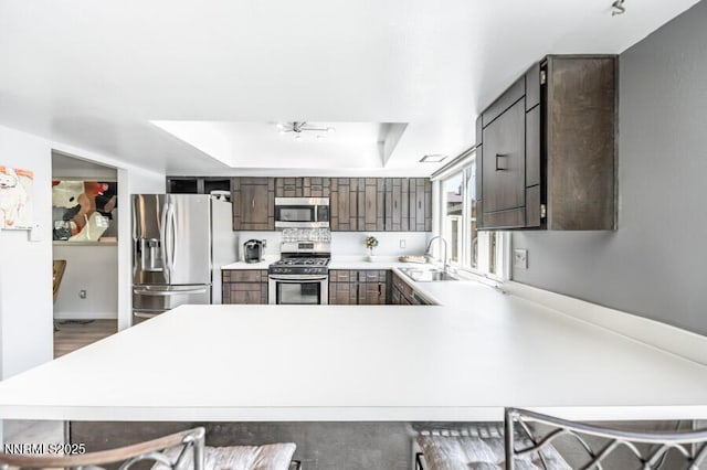 1419 Foster Dr, Reno, NV 89509 - kitchen featuring appliances with stainless steel finishes, a peninsula, a tray ceiling, light countertops, and dark brown cabinetry